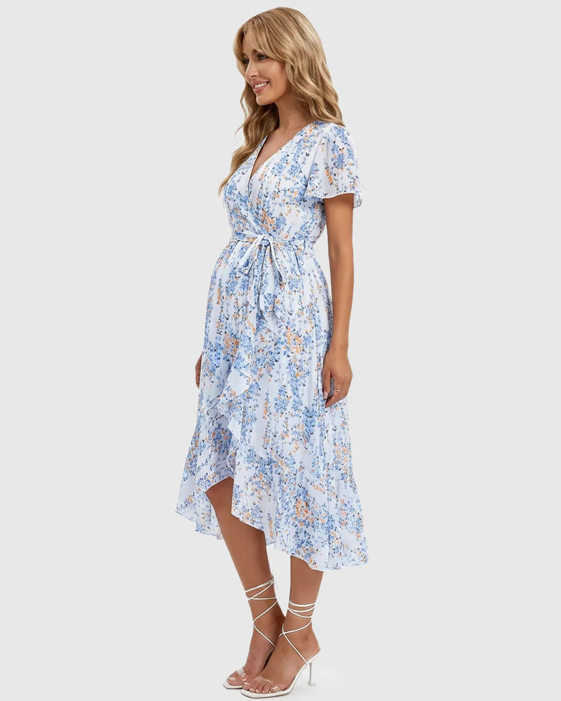 Smiling pregnant woman in a light blue floral V-neck midi dress with ruffled hem and tie-waist.
