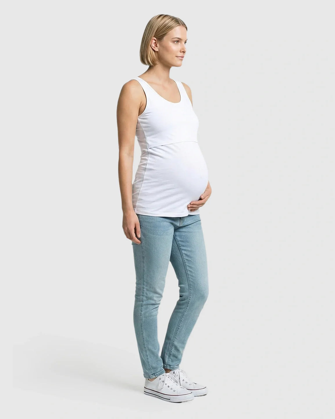 Pregnant woman in white stretch nursing-access maternity tank top and light blue jeans.