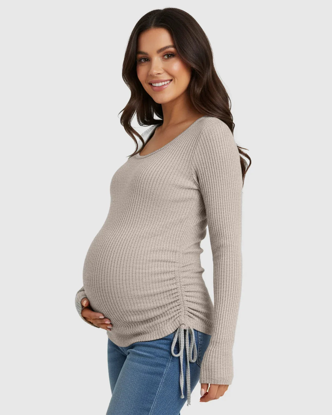 Smiling pregnant woman in a beige ribbed long-sleeve maternity top with adjustable side drawstrings and a U-neck.