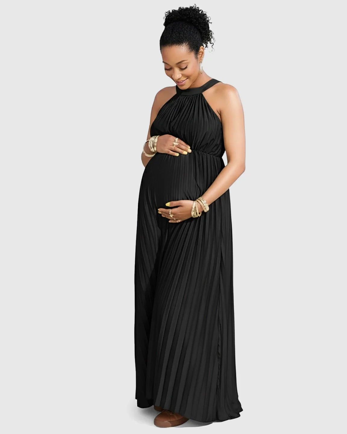 Pregnant woman in a black faux silk halter neck pleated maternity maxi dress, holding her belly.