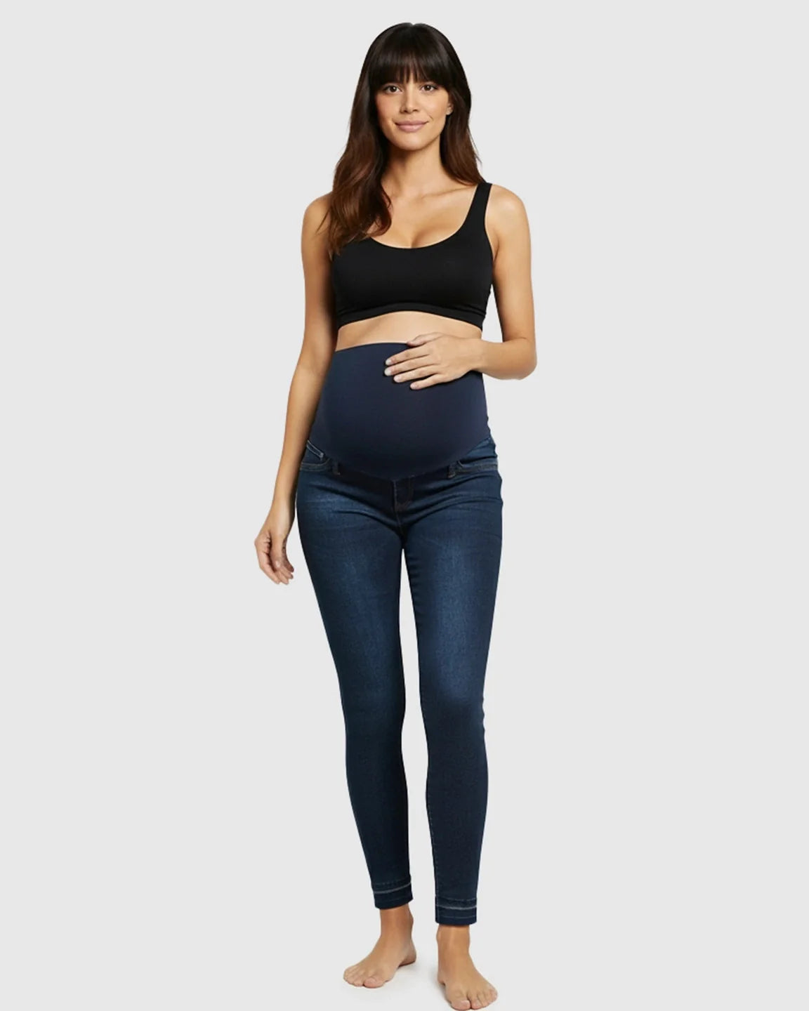 Woman in dark wash, high-waist skinny maternity jeans with a supportive elastic belly band.