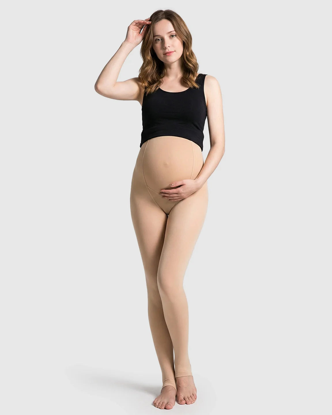 Pregnant woman modeling nude fleece-lined over-bump maternity leggings with stirrups and a black tank top.