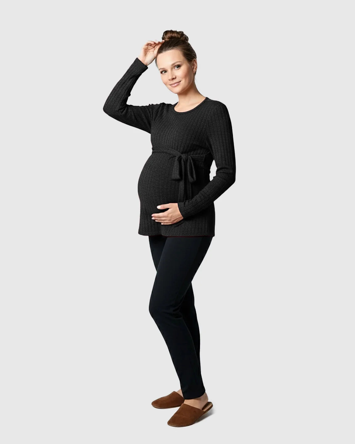 Maternity model in a black ribbed tie-waist long sleeve sweater and black pants, holding her baby bump.