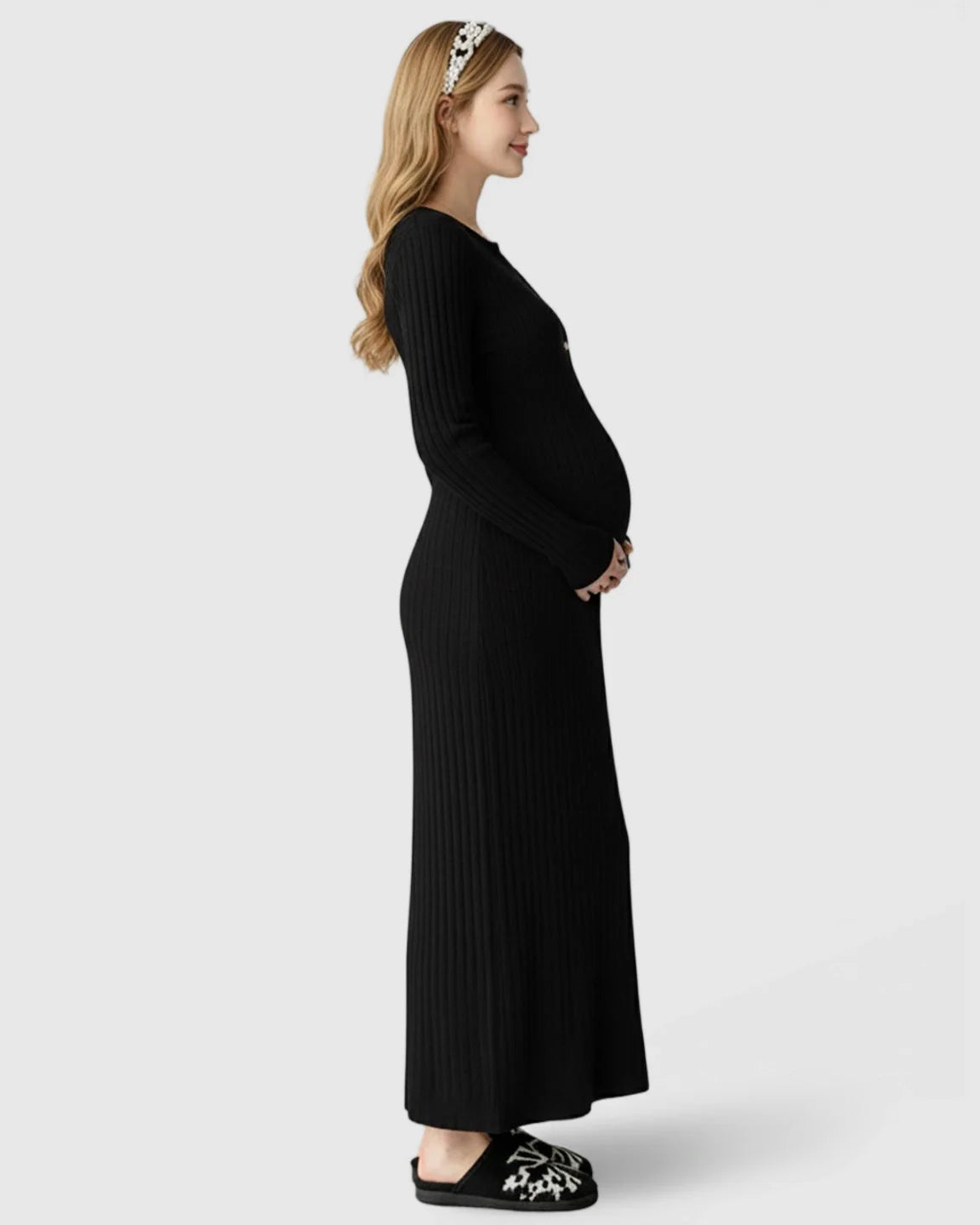 Maternity maxi dress in black ribbed knit, A-line shape, long sleeves, worn by a pregnant woman.