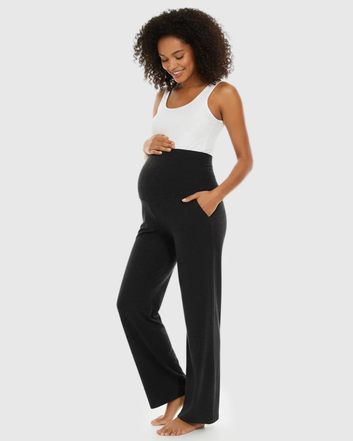 Smiling pregnant woman in black wide-leg maternity lounge pants with a foldable waistband and side pockets.