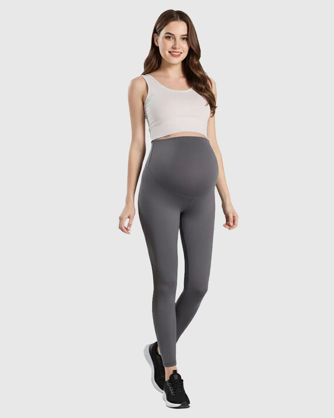 Smiling pregnant woman wearing gray double-layer belly support maternity leggings and a white crop top.