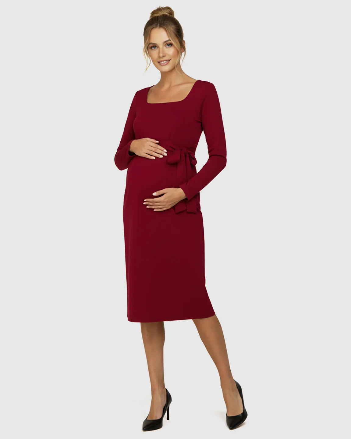 Pregnant woman in a red square-neck, long-sleeve bodycon maternity midi dress with a side-tie belt.