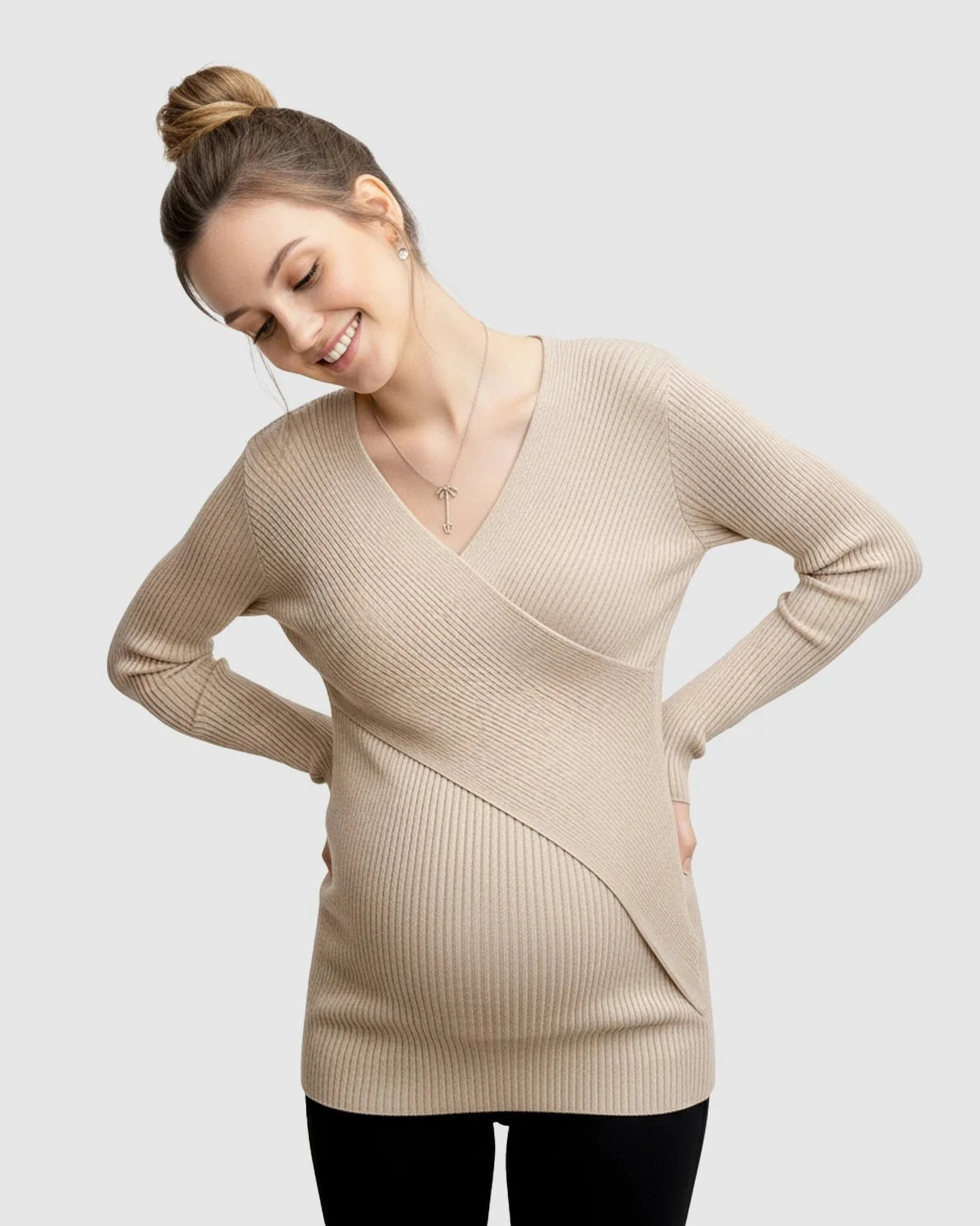 Smiling pregnant woman in a beige ribbed faux-wrap maternity top, hands on hips.