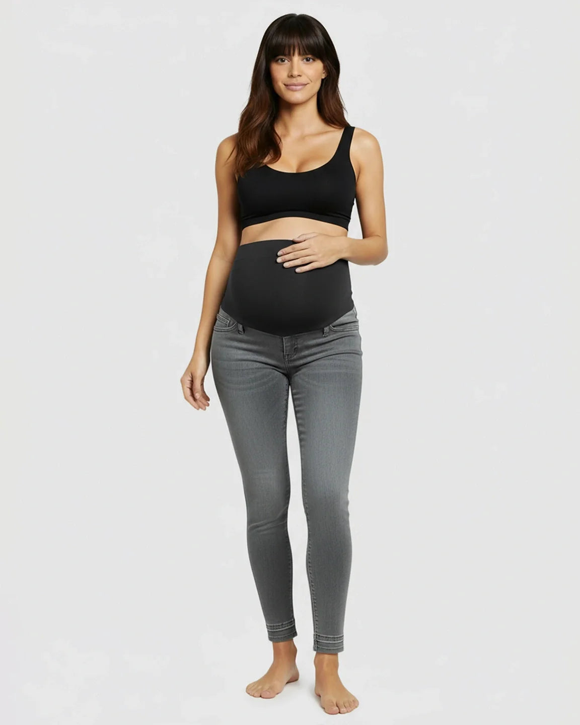 Woman in gray stretch high-waist skinny maternity jeans with a black elastic waistband and black bra.