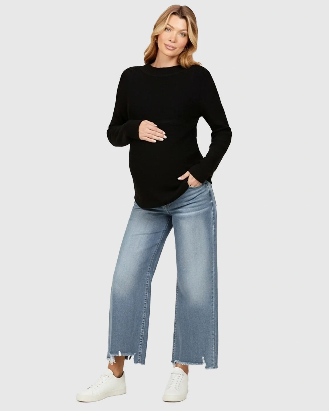 Woman in light wash wide-leg maternity jeans with raw hem, black long-sleeve top, and white sneakers.