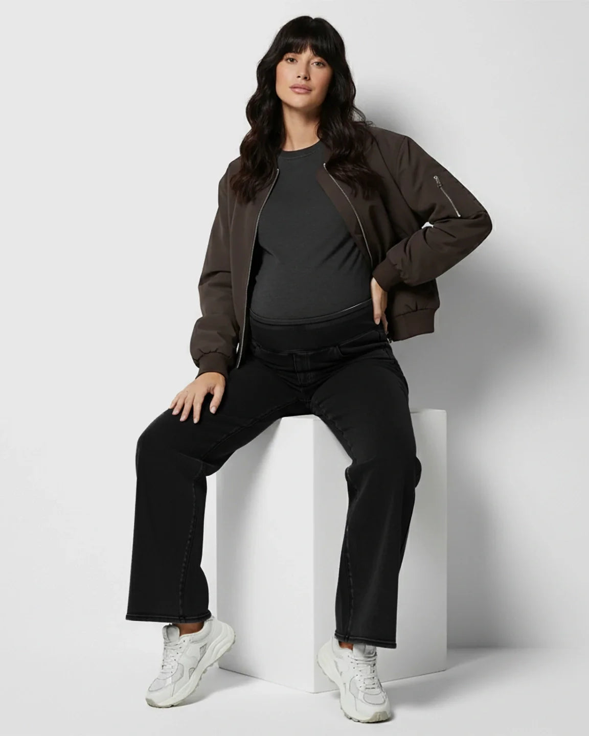 Maternity model wearing black high-waist wide-leg denim jeans with a stretchy belly band, dark tee, and bomber jacket.