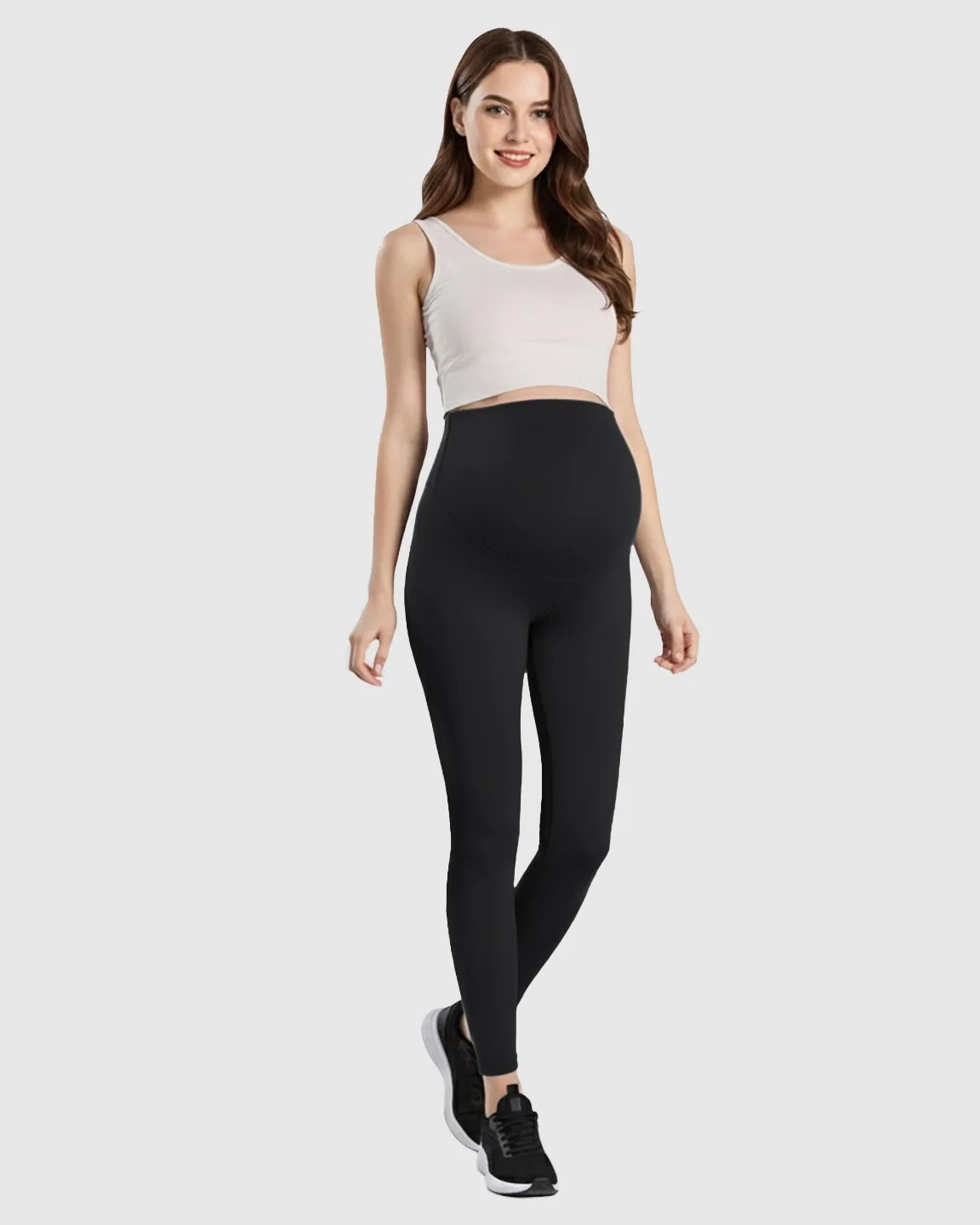 Smiling pregnant woman in black double-layer belly support maternity leggings and white crop top.