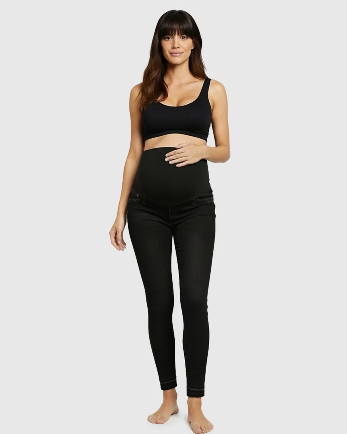 Smiling pregnant woman models black high-waist skinny maternity jeans with an elastic belly band.