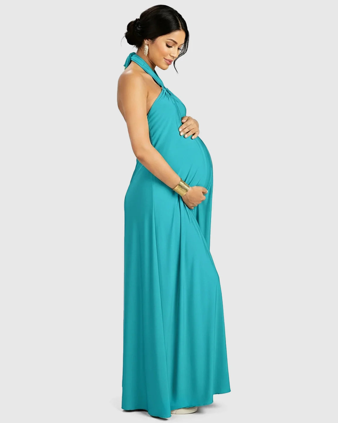 Pregnant woman in a turquoise backless halter neck chiffon maternity maxi dress, gently cradling her bump.