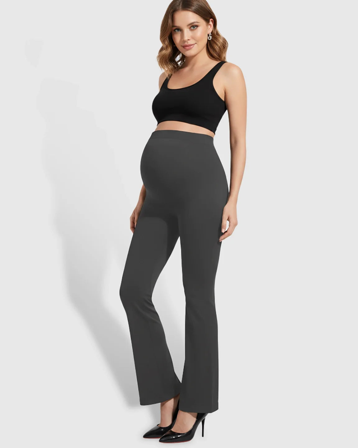 Pregnant woman in black crop top and charcoal gray over-belly bootcut maternity pants with a soft flare.