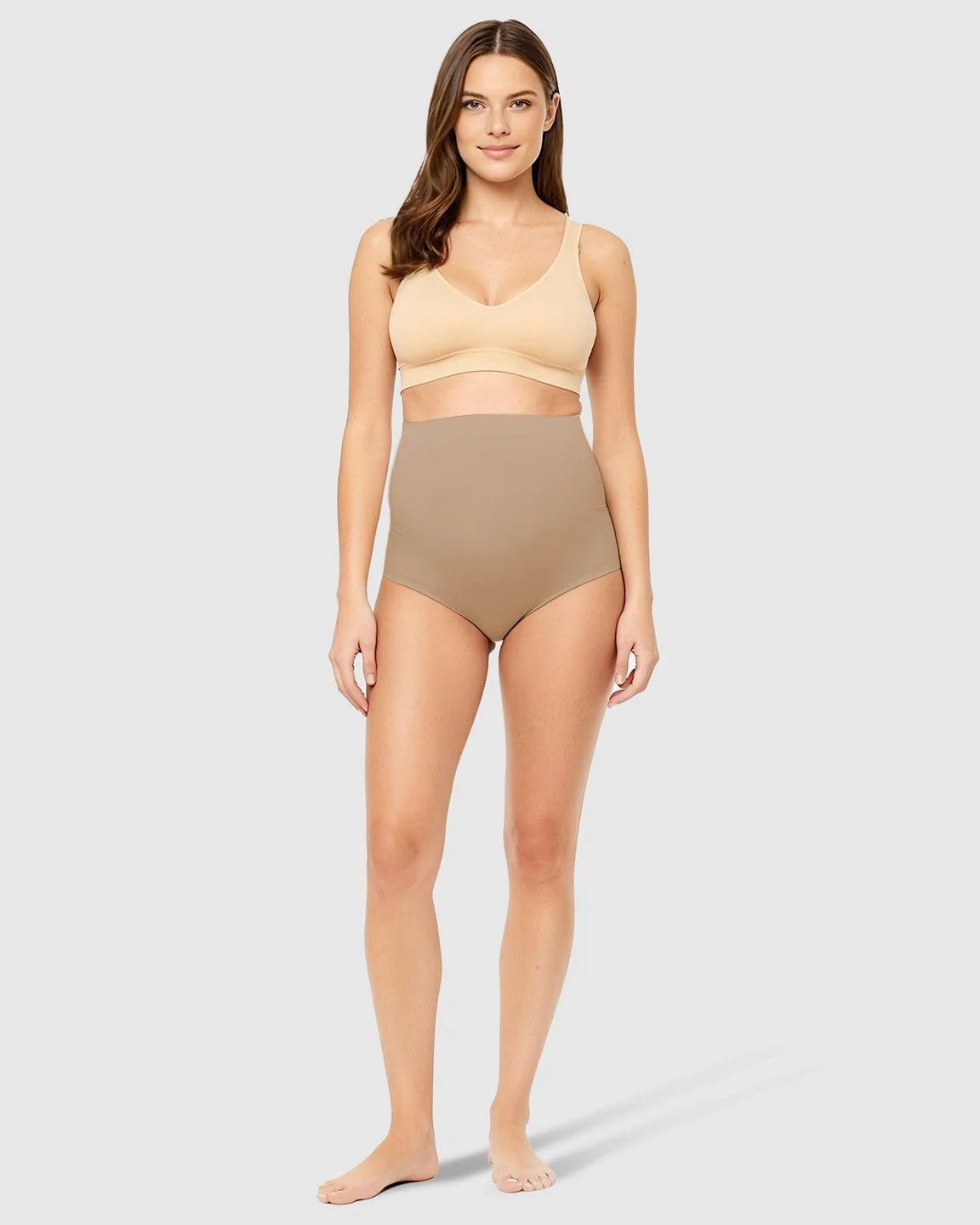 Woman in nude high-waist seamless belly-support maternity underwear and matching bra, full body.