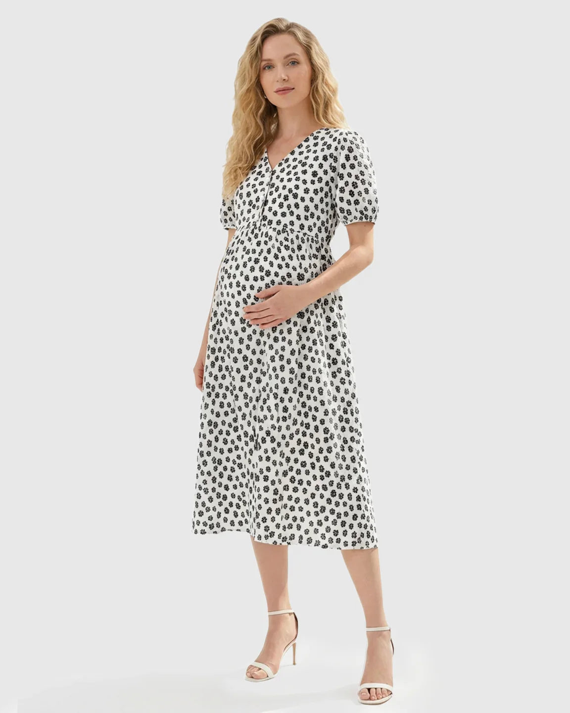 Maternity nursing dress: white midi with black floral print, V-neck, button-front, short sleeves, on a pregnant model.