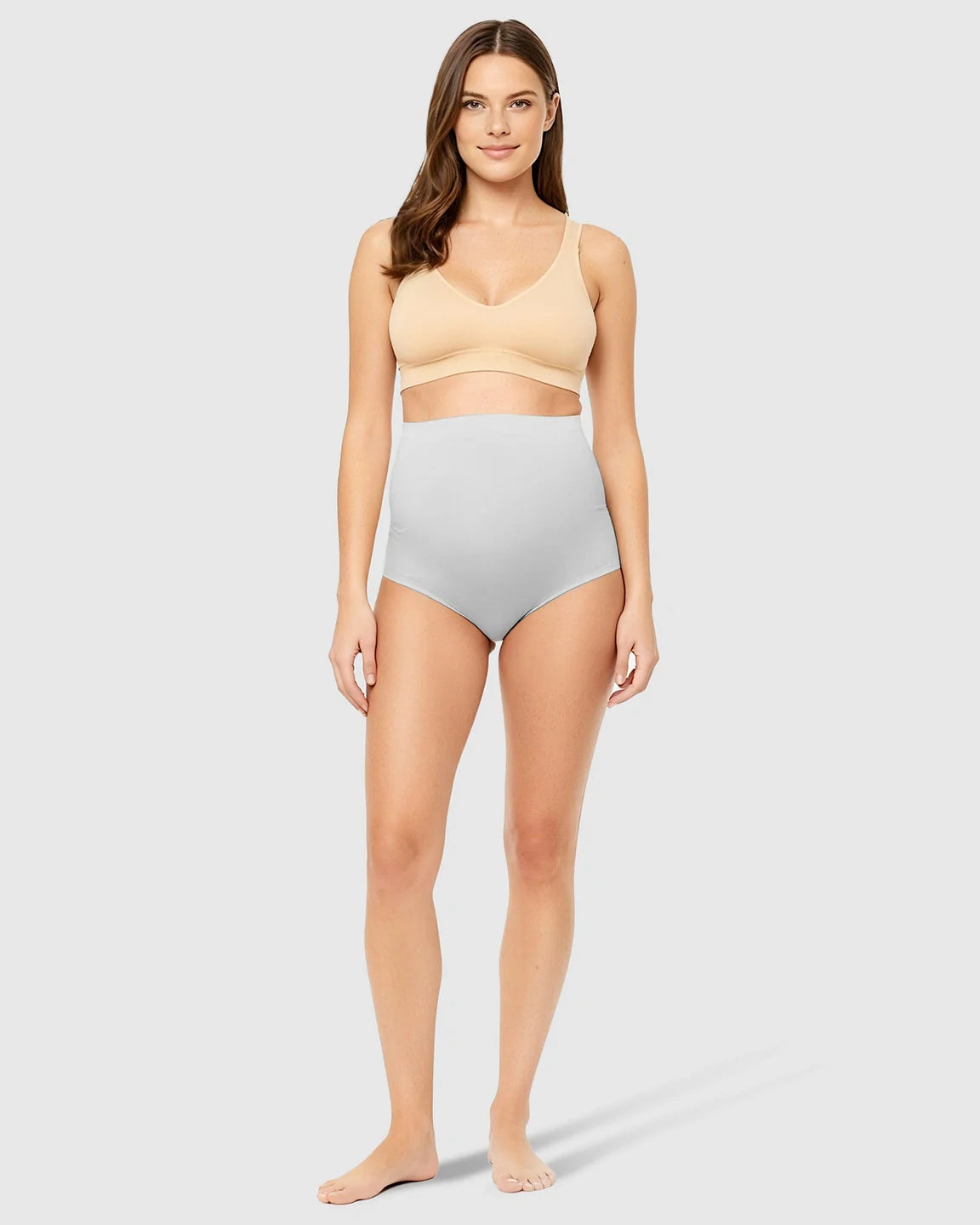 Woman modeling light grey high-waist seamless belly-support maternity underwear with a nude bra.
