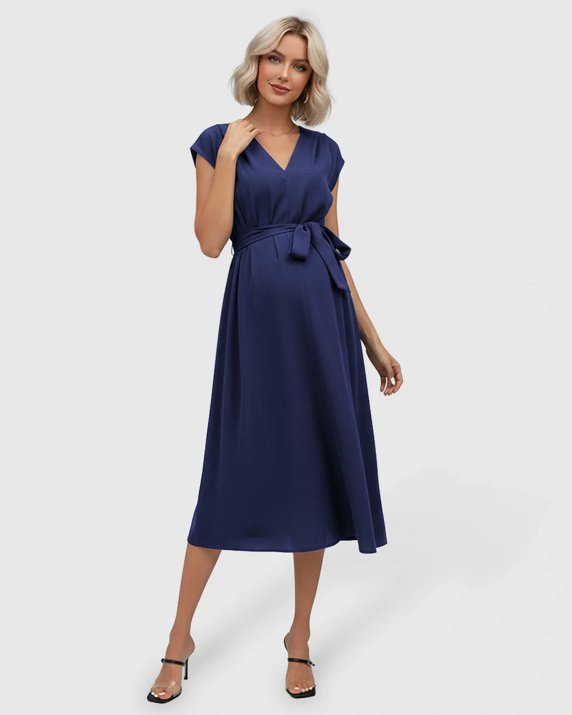 Blonde model in a navy blue V-neck maternity midi dress with flutter sleeves and an adjustable tie-waist.