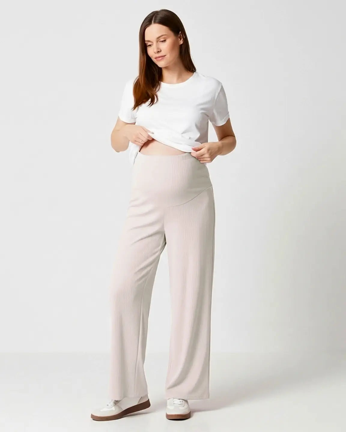 Woman in soft beige wide-leg stretch maternity pants with an over-bump waistband and white t-shirt.