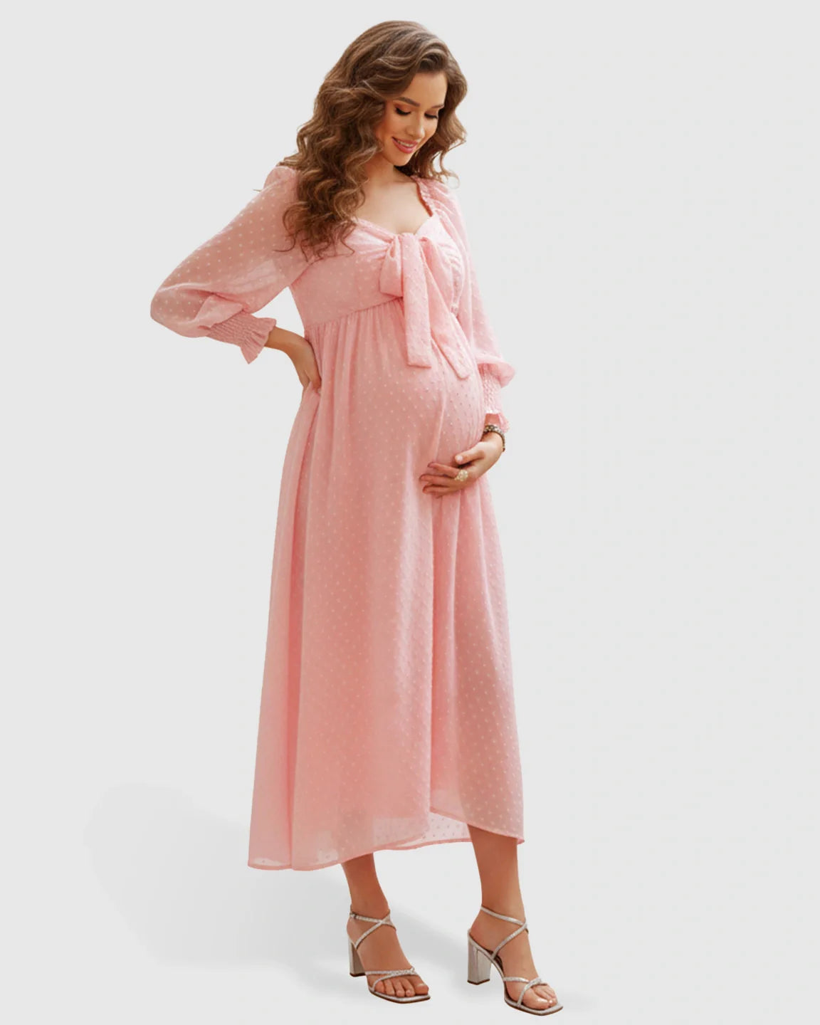 Pregnant woman in a pink polka-dot chiffon long-sleeve maternity maxi dress with a square neckline and bow.