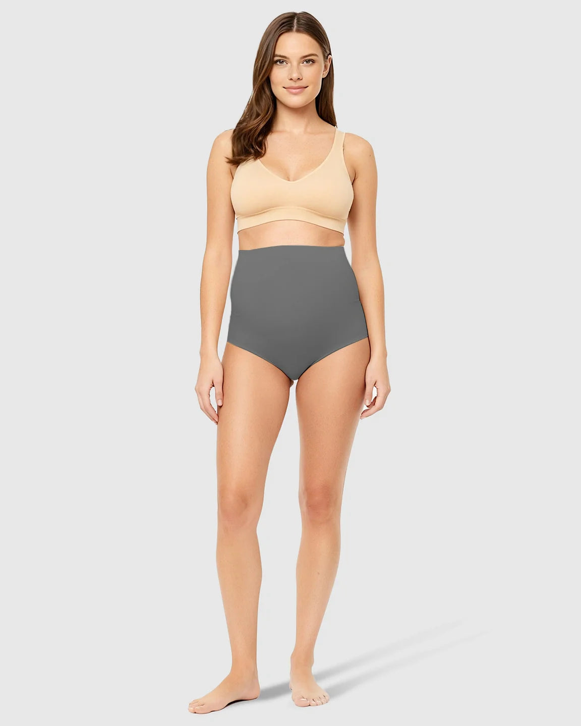 Woman modeling gray high-waist seamless maternity underwear with belly support and a nude bra.