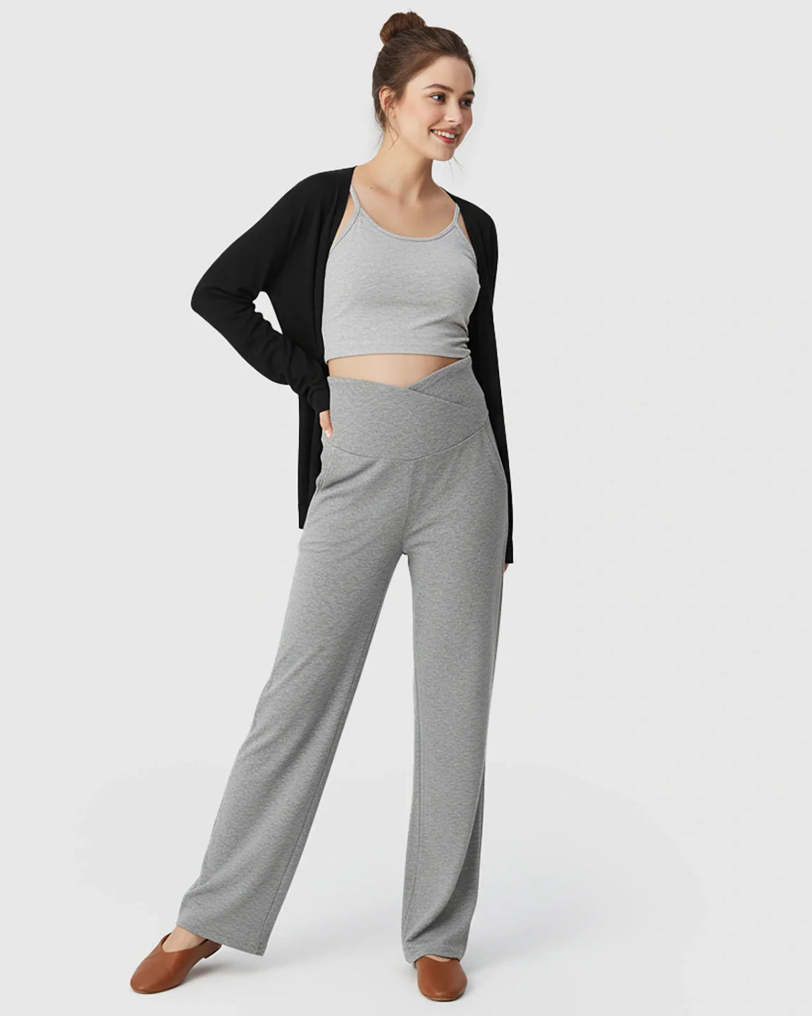 Smiling woman in gray crossover waist wide-leg maternity lounge pants, gray crop top, and black cardigan.