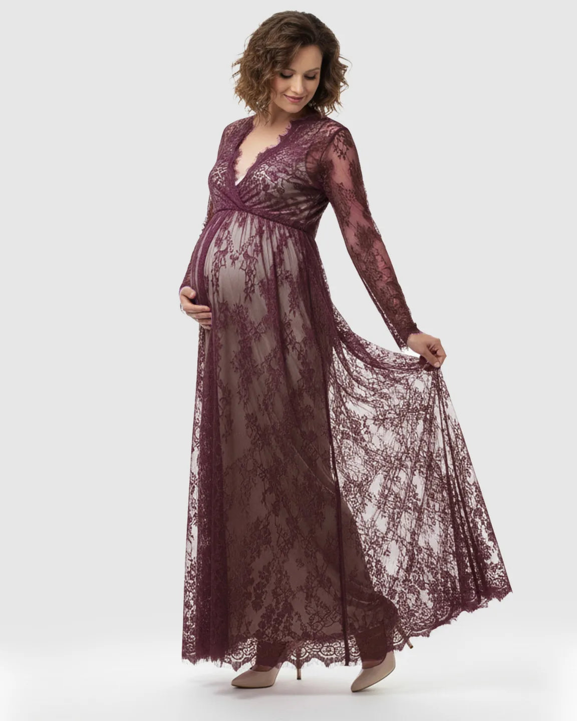 Maternity model in a sheer floral lace empire waist maxi dress in deep plum, with long sleeves and a flowing skirt.