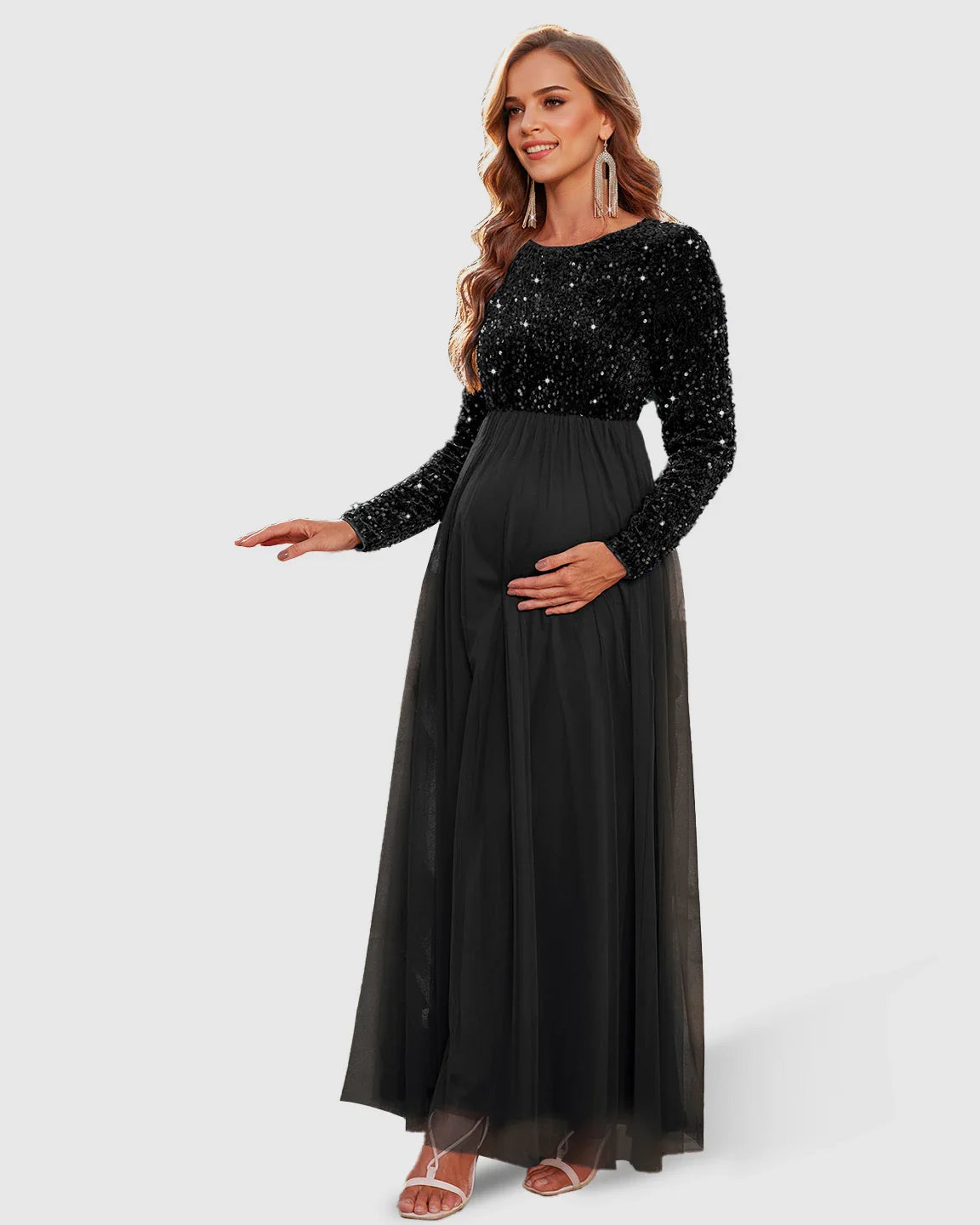 Pregnant woman in a black sequin long-sleeve empire waist maternity maxi dress with a flowing mesh skirt.