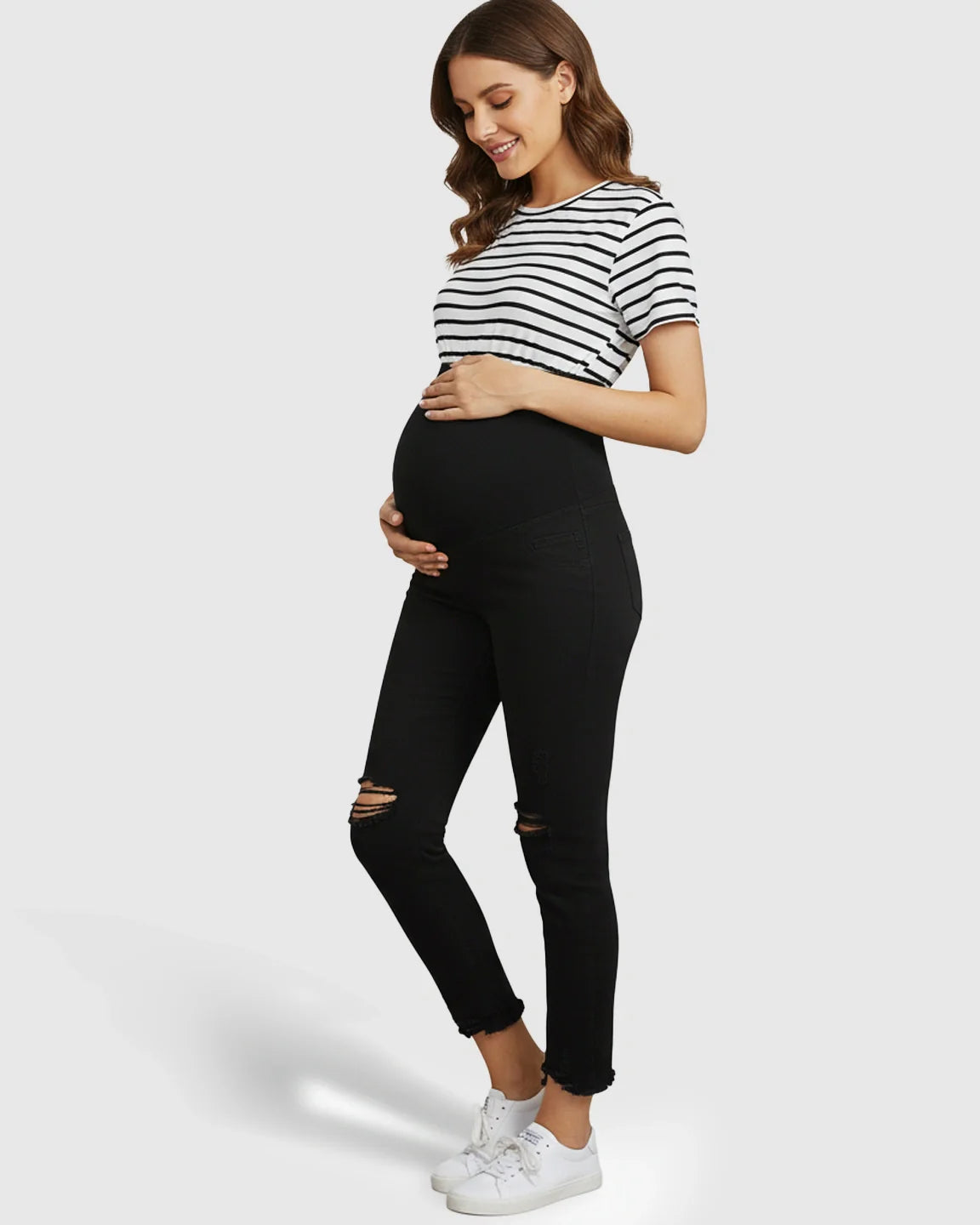 Smiling pregnant woman in black ripped maternity skinny jeans with over-belly panel and a striped t-shirt.