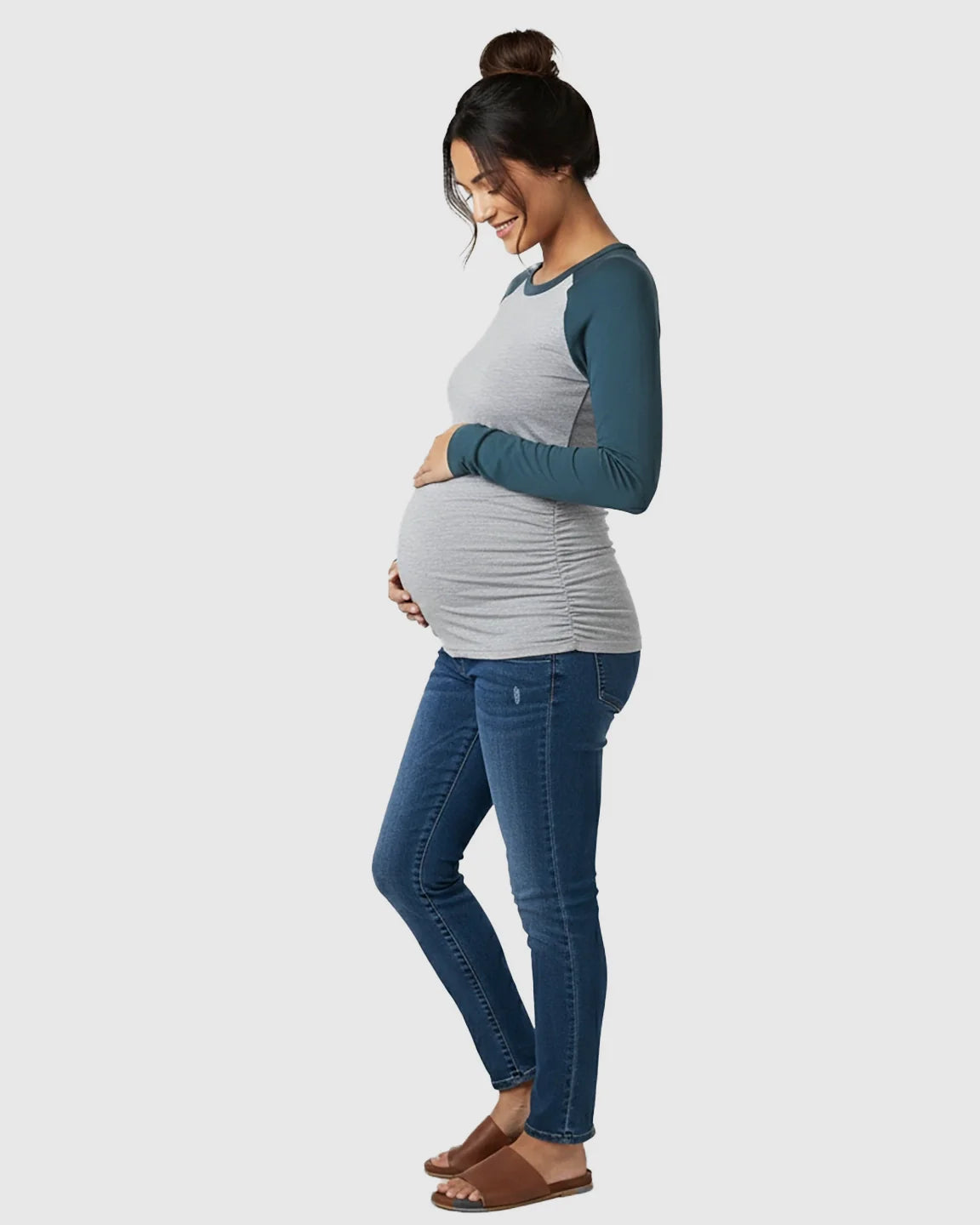 Pregnant woman in a gray and teal raglan sleeve maternity top with ruched sides and dark wash jeans.
