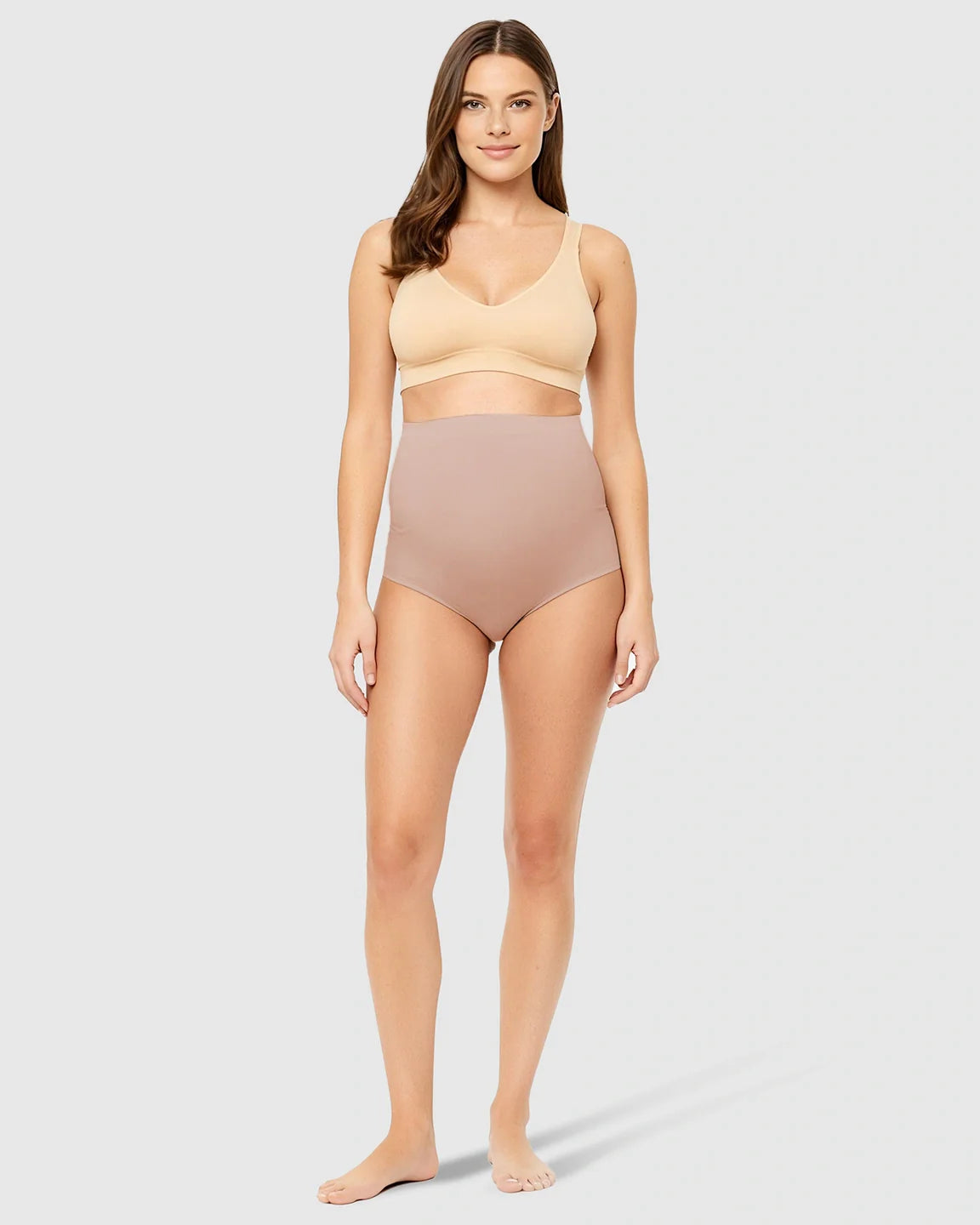Woman in nude high-waist seamless maternity underwear and matching bra, offering gentle belly support.
