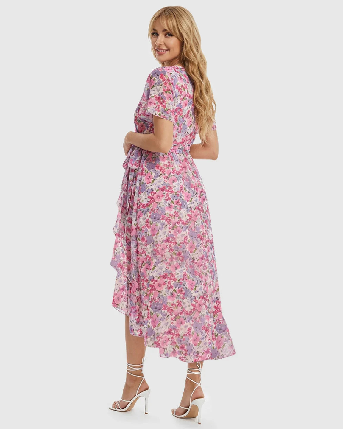 Blonde model in a pink floral V-neck maternity midi dress with ruffled high-low hem and white heels.