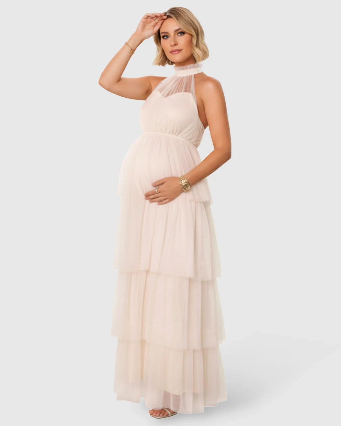 Blonde pregnant woman in a cream halter neck tiered mesh maternity gown.