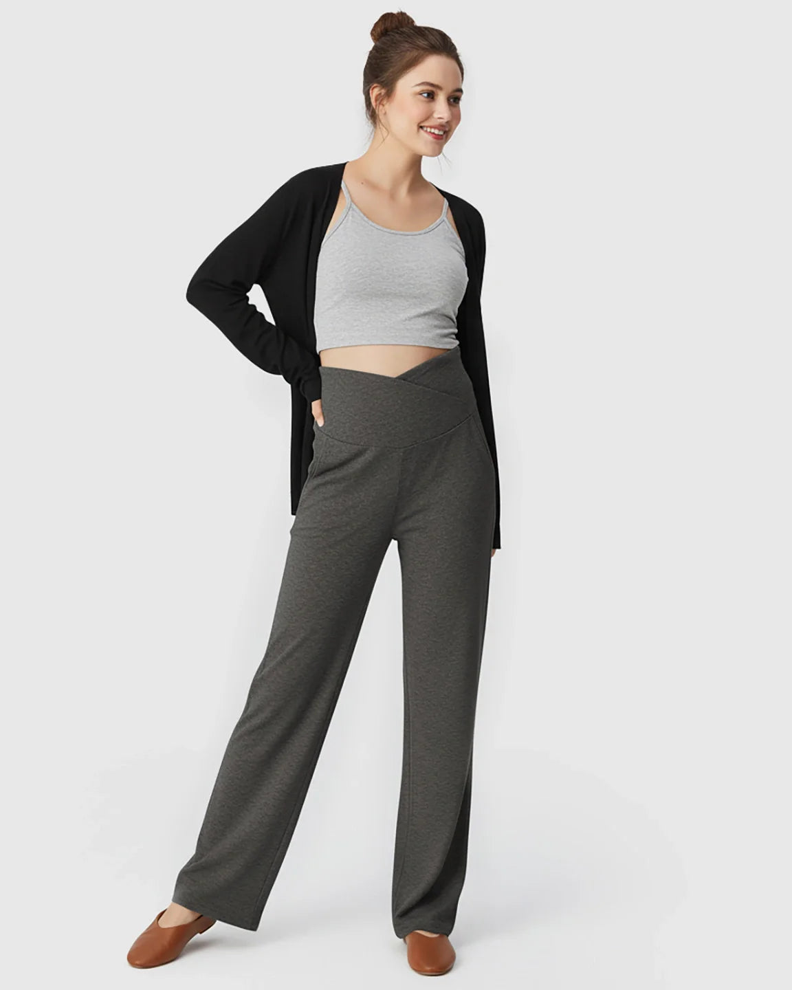 Smiling woman in charcoal crossover waist wide-leg maternity lounge pants, grey crop top, and black cardigan.