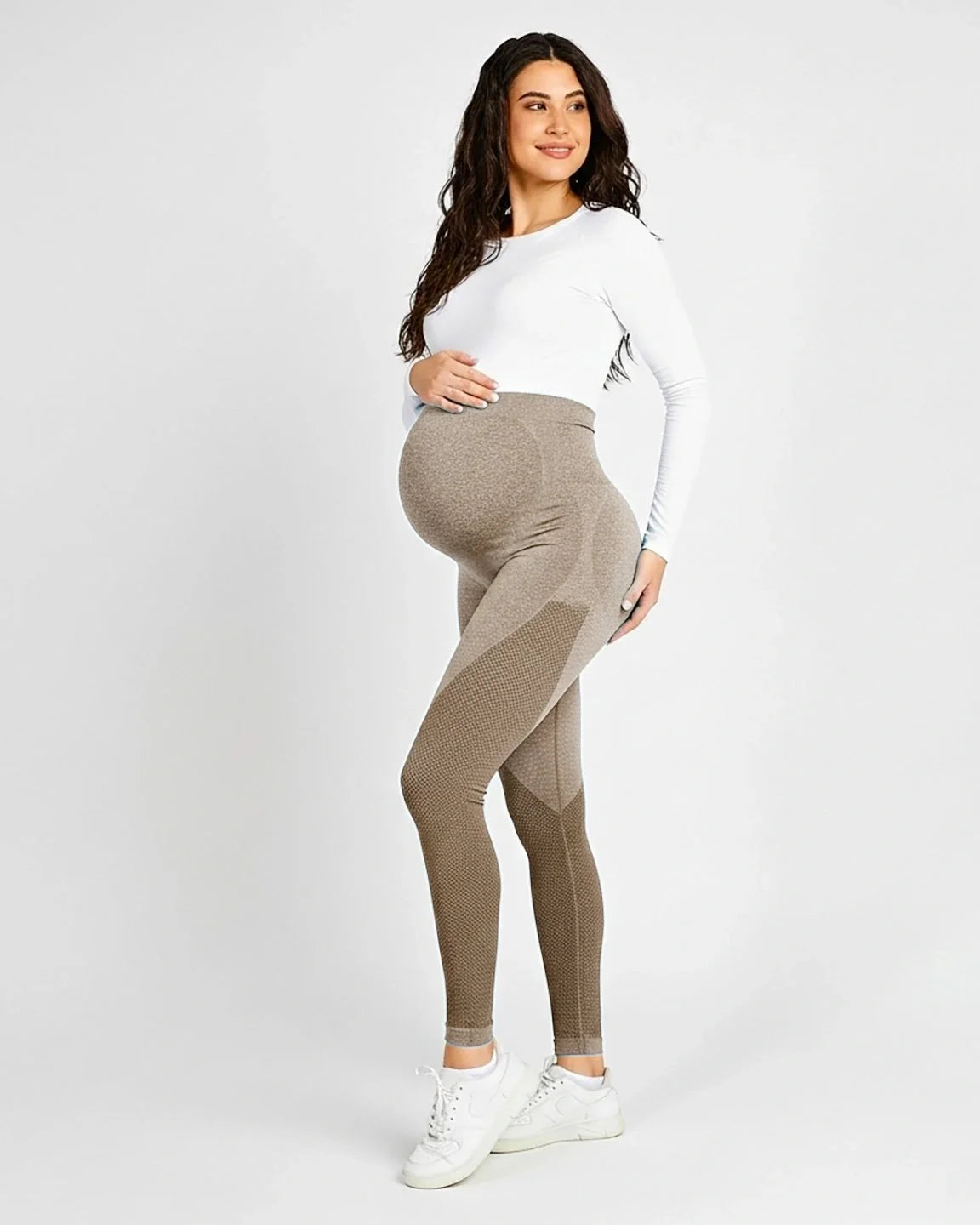 Pregnant woman in high-waisted, body-hugging taupe maternity leggings with textured details and a white long-sleeve top.