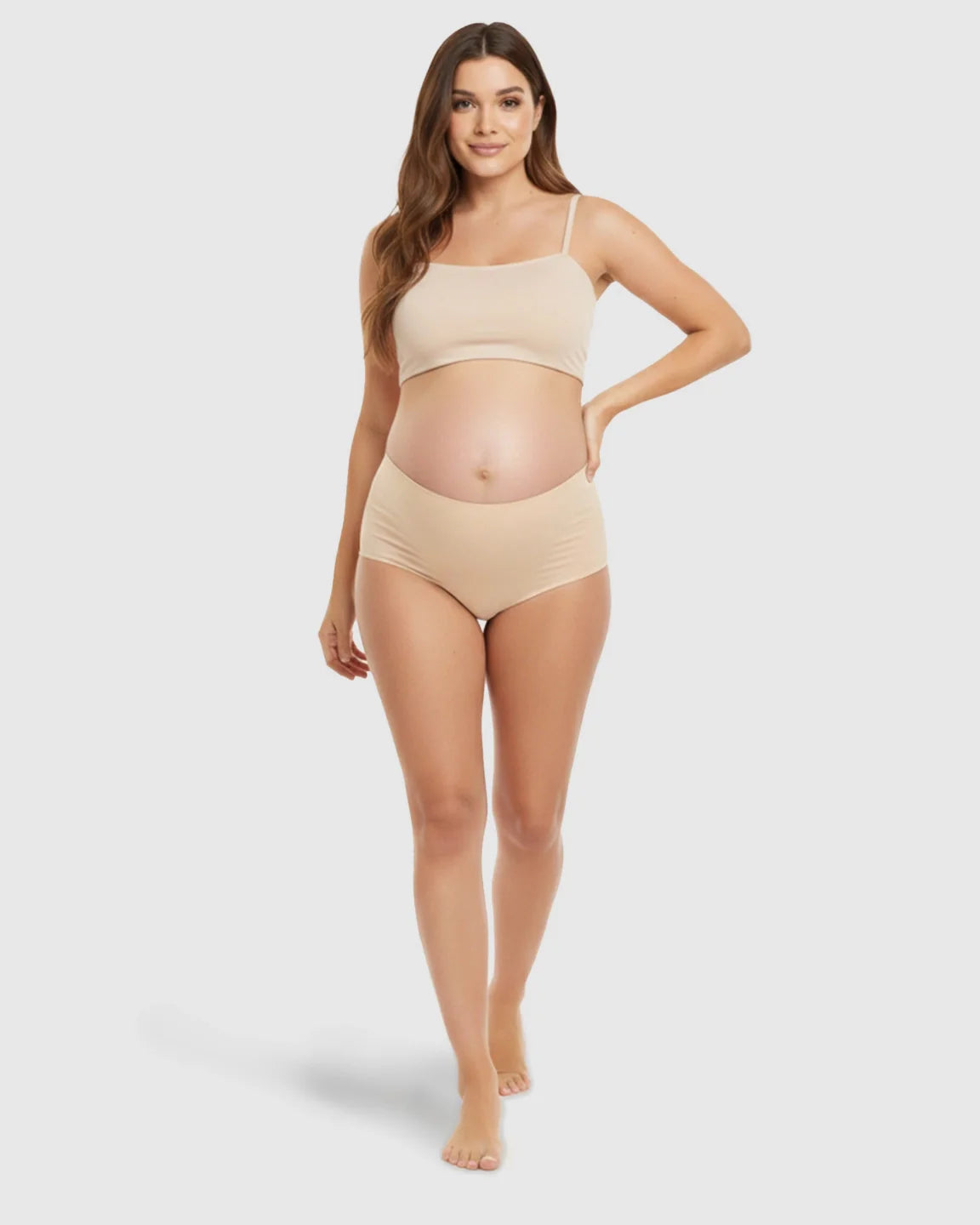 Pregnant woman modeling seamless nude high-waist maternity support underwear and matching bralette.