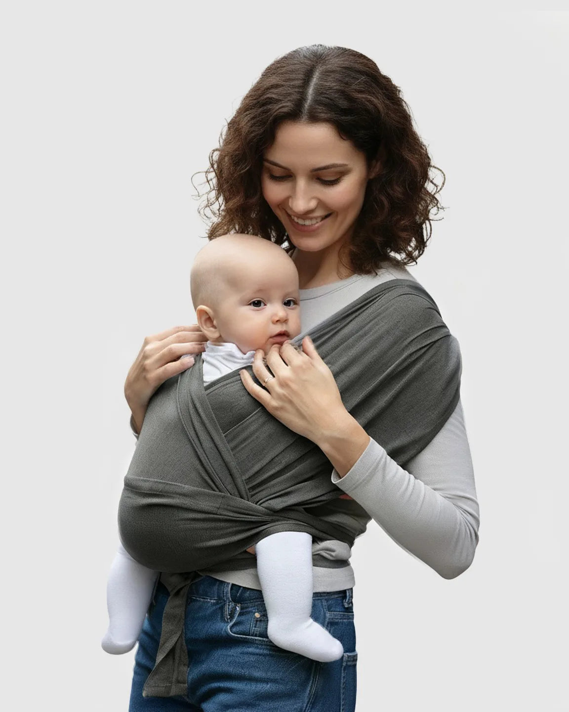 Woman smiling, wearing a dark gray adjustable wrap-around baby carrier with a baby snuggled close.