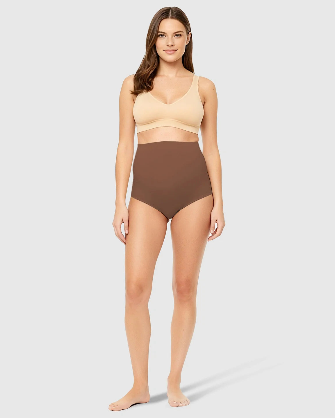 Woman in brown high-waist seamless maternity underwear and a beige bra, offering belly support.