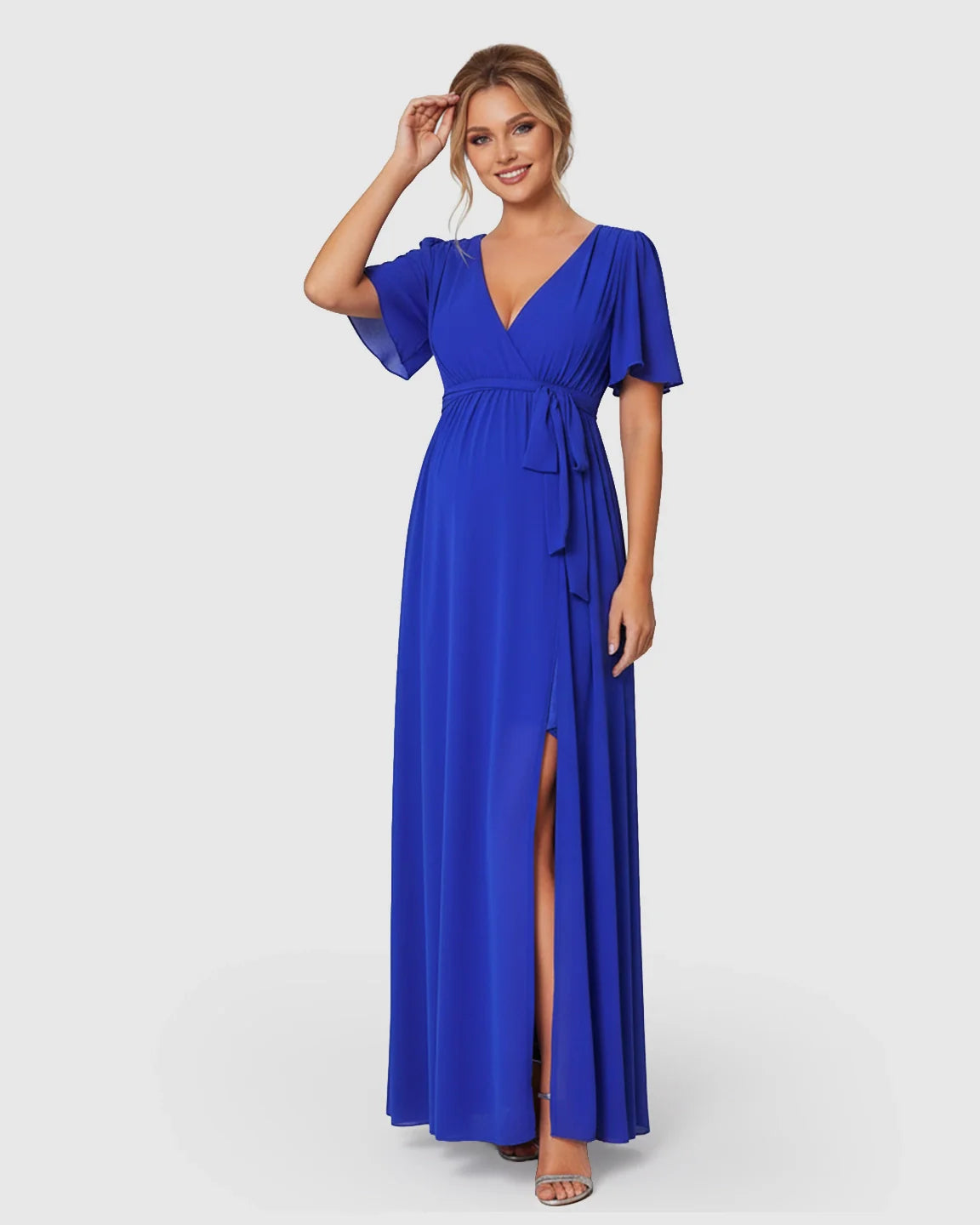Woman in a royal blue surplice V-neck flutter sleeve maternity maxi dress with a front slit and waist tie.