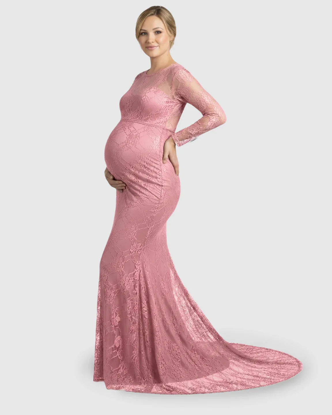 Pregnant woman in a pink sheer lace trumpet maternity gown with long sleeves and a mermaid-style skirt.