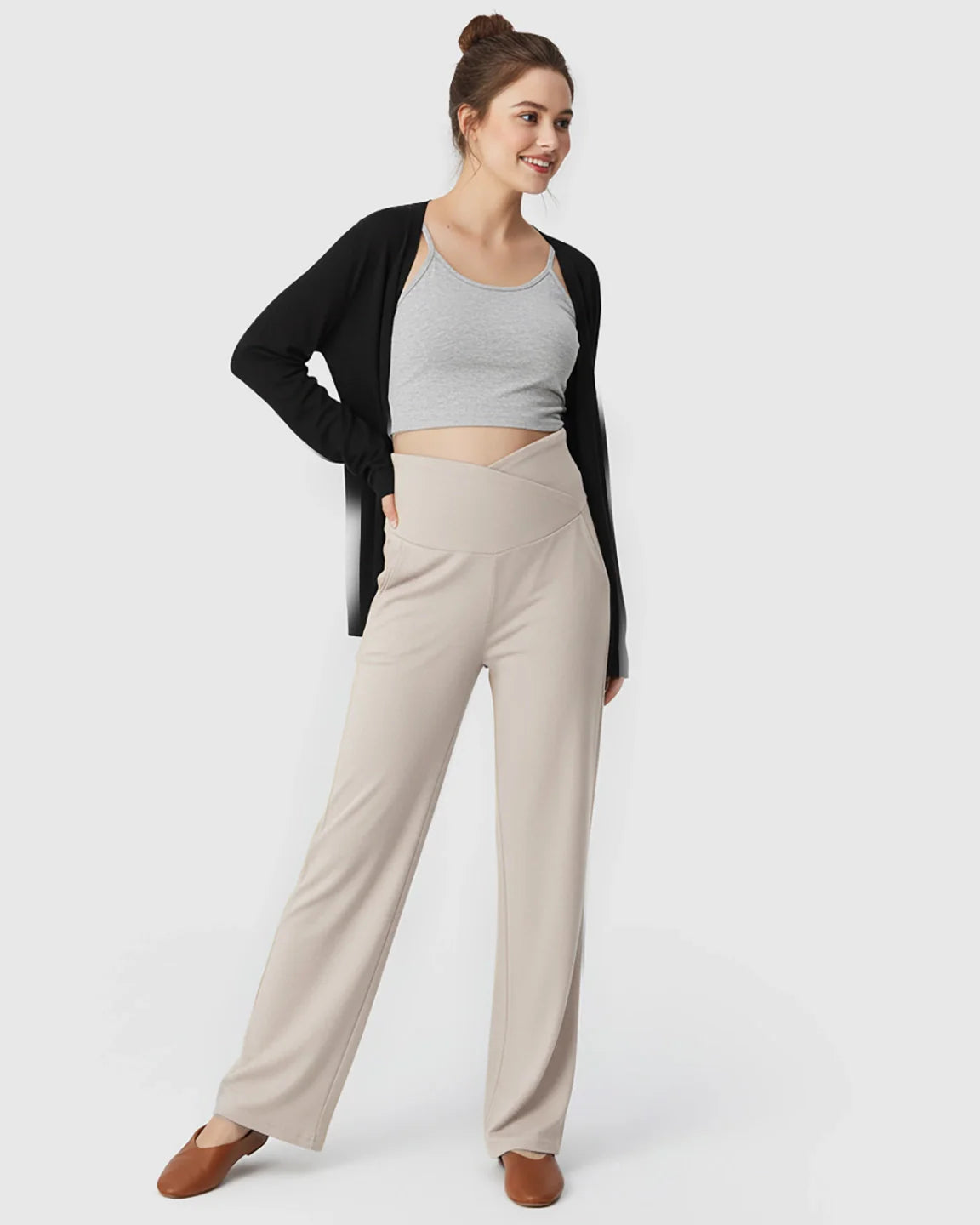 Smiling woman in beige crossover waist wide-leg maternity lounge pants, grey crop top, and black cardigan.