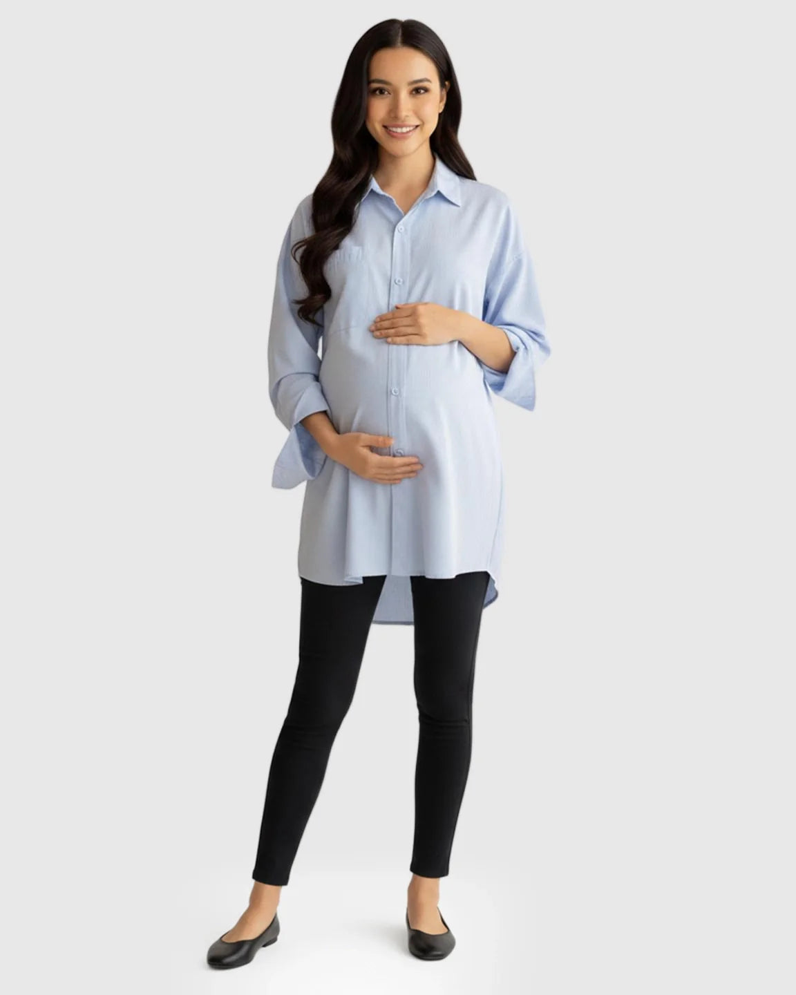 Smiling pregnant woman in a light blue cotton lapel-collar button-front maternity tunic and black leggings.