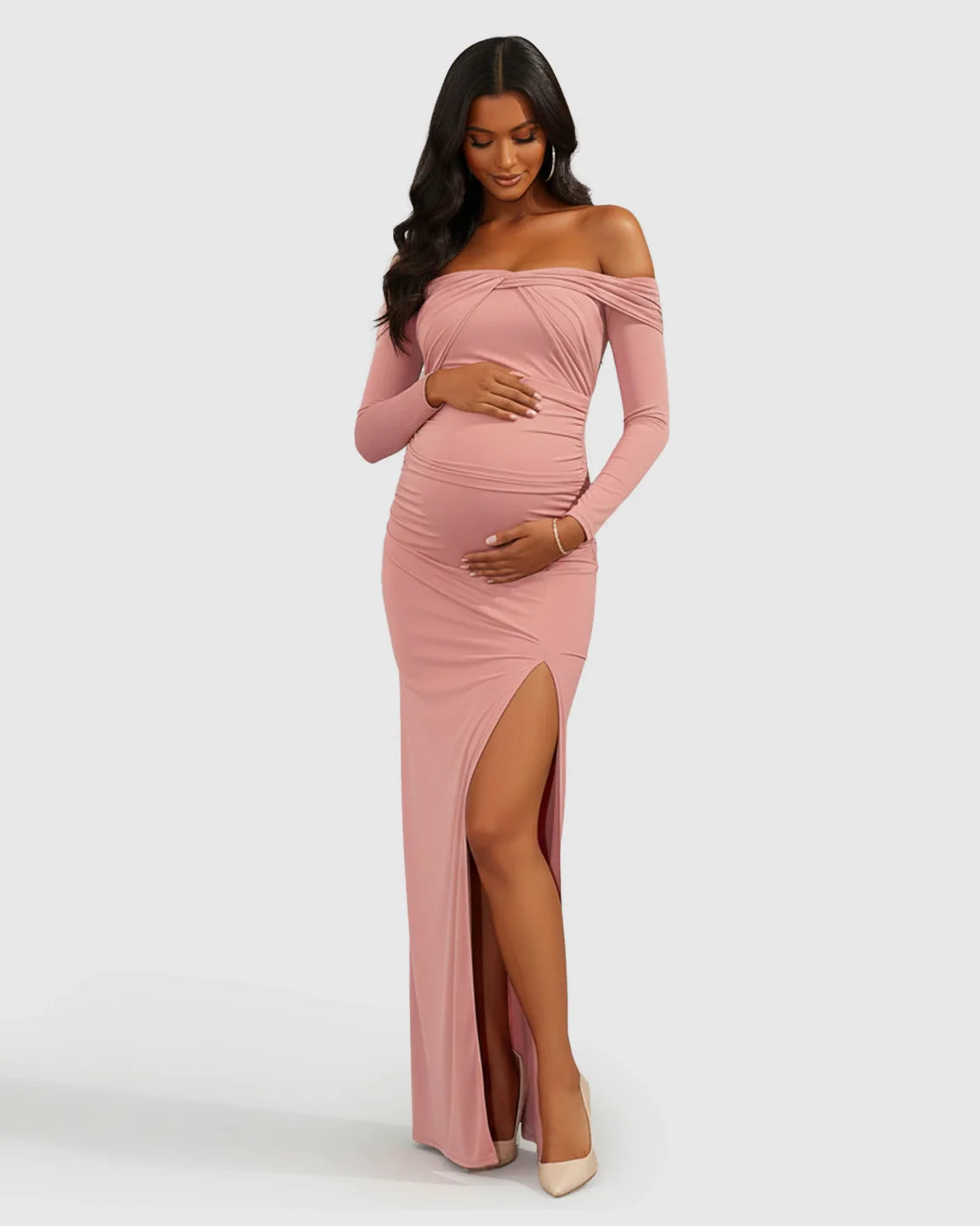 Maternity model in a pink ruched off-shoulder bodycon dress with long sleeves and a high slit.