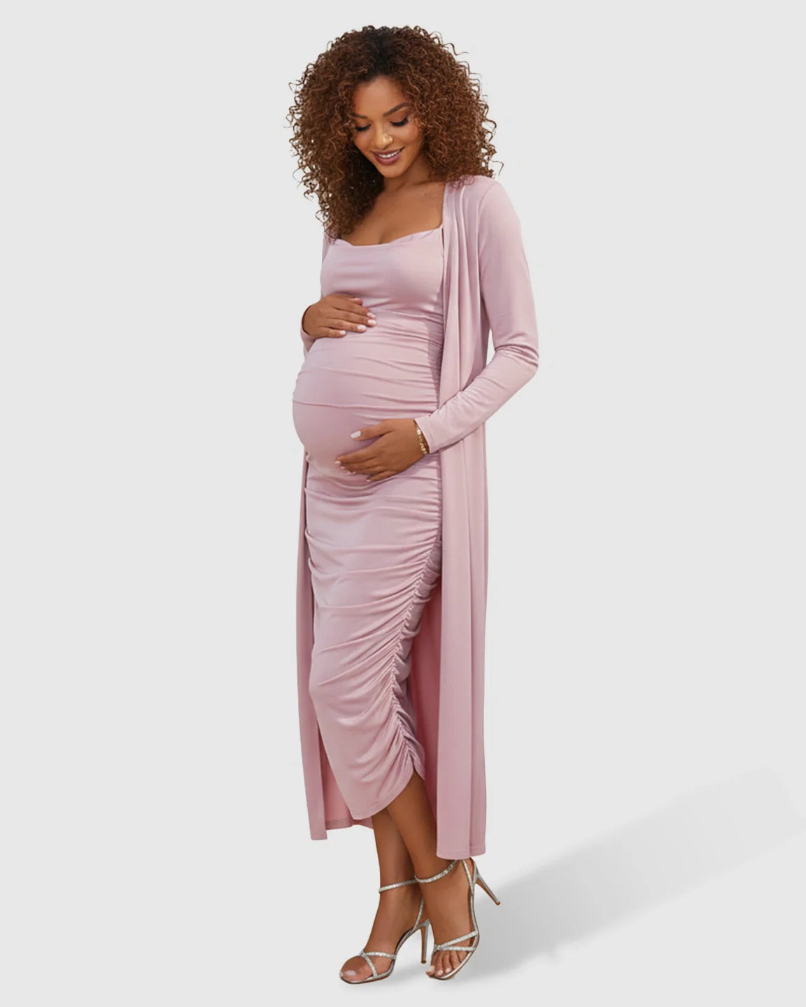 Pregnant woman in a pink side-ruched slip dress and long-sleeve cardigan maternity set.