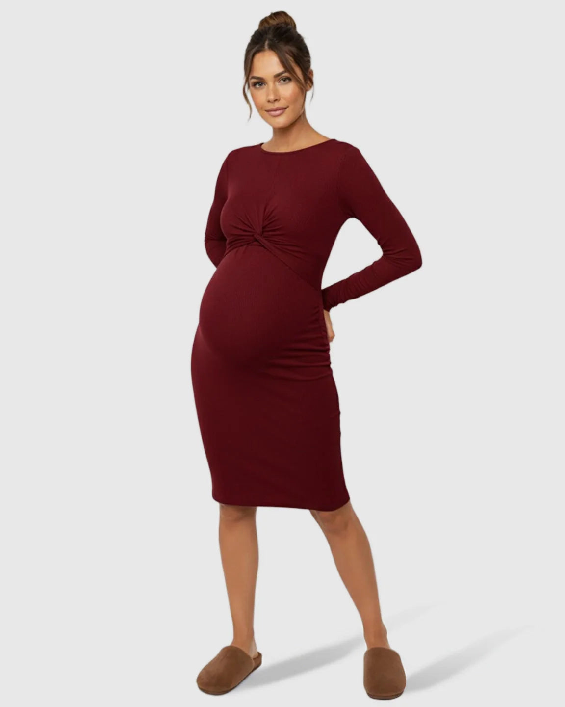 Maternity model in a long-sleeve, burgundy ribbed bodycon dress with a twist-front detail and empire waist.