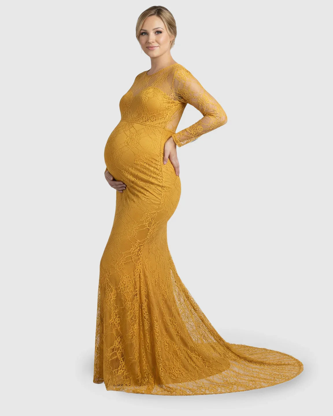 Smiling pregnant woman in a mustard sheer lace trumpet maternity photoshoot gown with long sleeves.