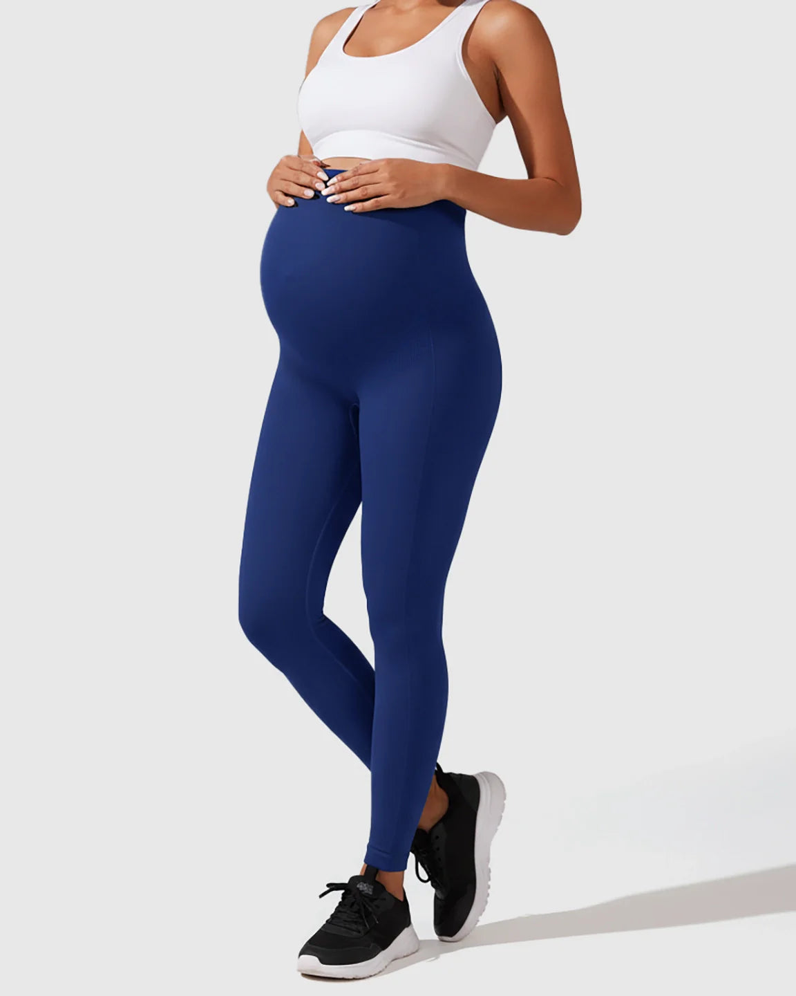 Pregnant woman in seamless navy blue high-waisted maternity leggings and a white sports bra.