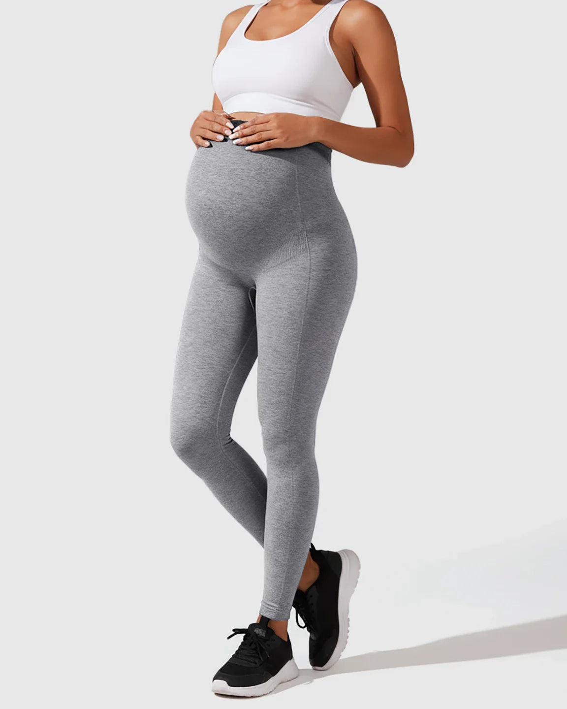 Pregnant woman wearing heather gray seamless M-shape maternity leggings with a high-waisted, full-belly support design.