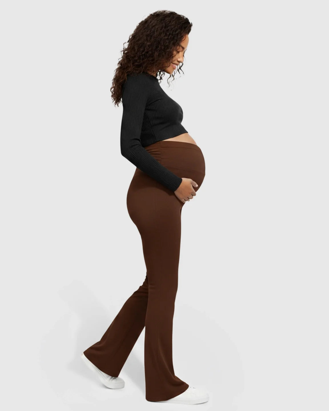 Pregnant woman in brown Bump Society flared maternity pants with a crossed waistband.